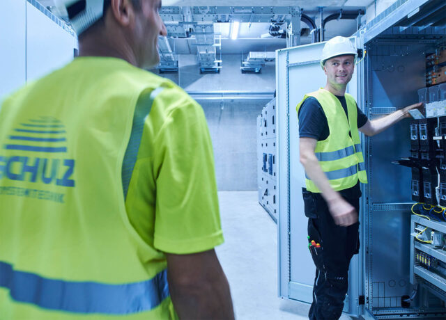 Techniker im Schaltraum prüfen gemeinsam einen geöffneten Schaltschrank.
