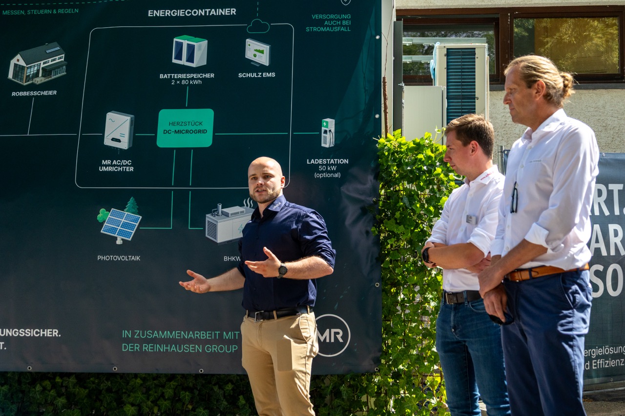 Projektbeteiligte erklären das Energiekonzept vor einer Infografik zum DC-Microgrid und Batteriespeicher.