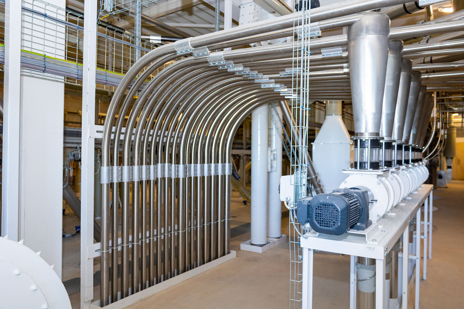 Ein Elektromotor treibt einen Vakuumförderer an, der über mehrere Rohrleitungen in eine industrielle Anlage integriert ist.