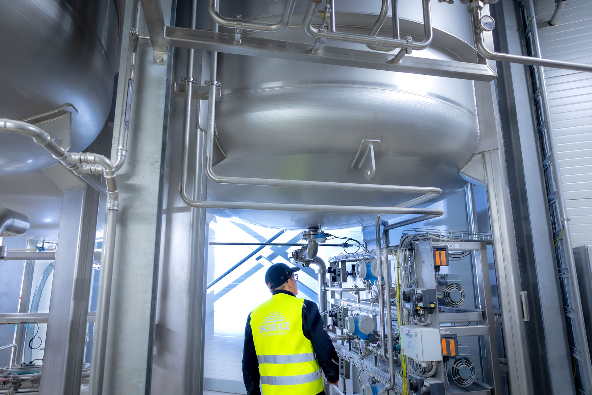 Eine Person steht vor einer großen industriellen Anlage mit Rohren und Tank.