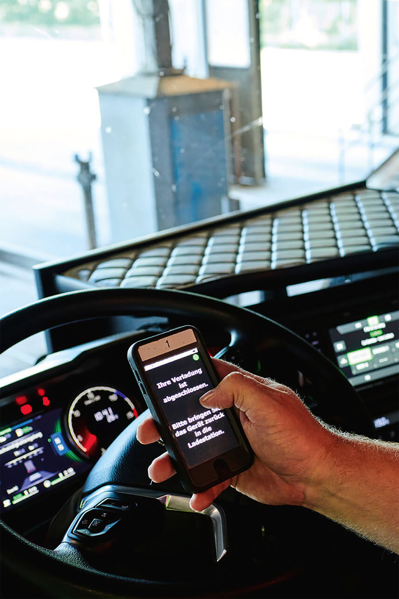 Ein Fahrer sitzt im Fahrzeug und liest auf einem mobilen Gerät die Meldung über den abgeschlossenen Ladevorgang.