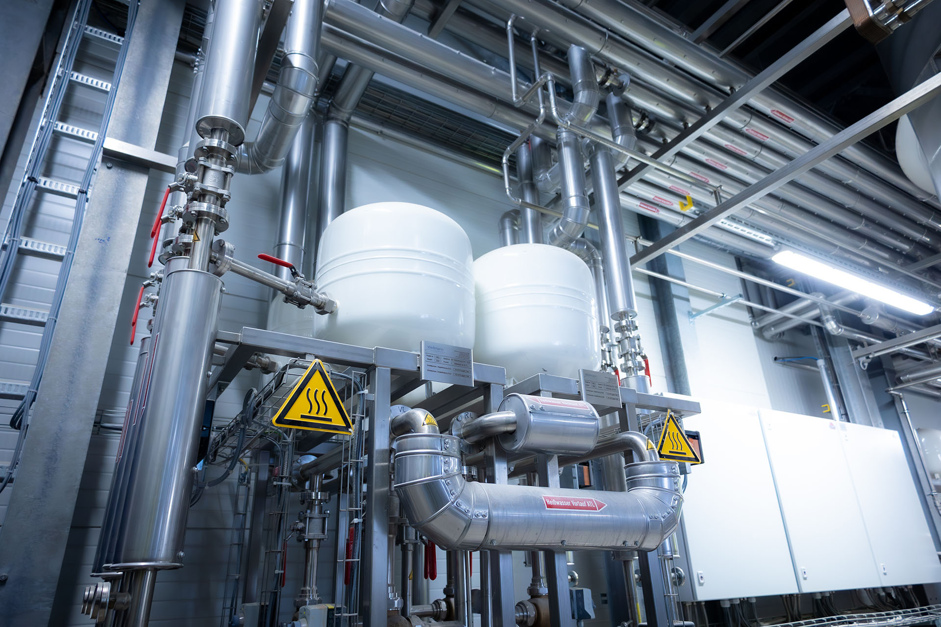 Industrielle Anlage mit Tanks, Rohren und Warnschildern in einem Innenraum.