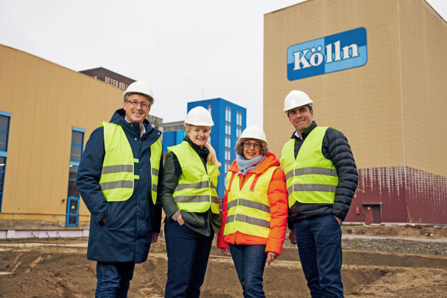 Vier Personen mit Schutzhelmen vor der neuen Produktionsstätte von Kölln.