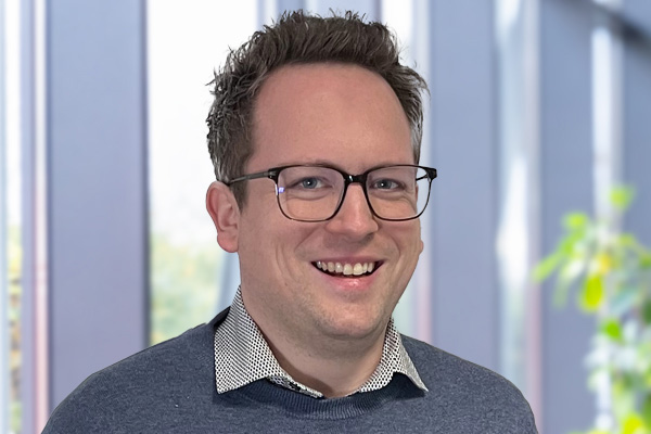 Joshua Schulz, Projektleiter Industrieautomation, vor einer Fensterfront im Foyer.